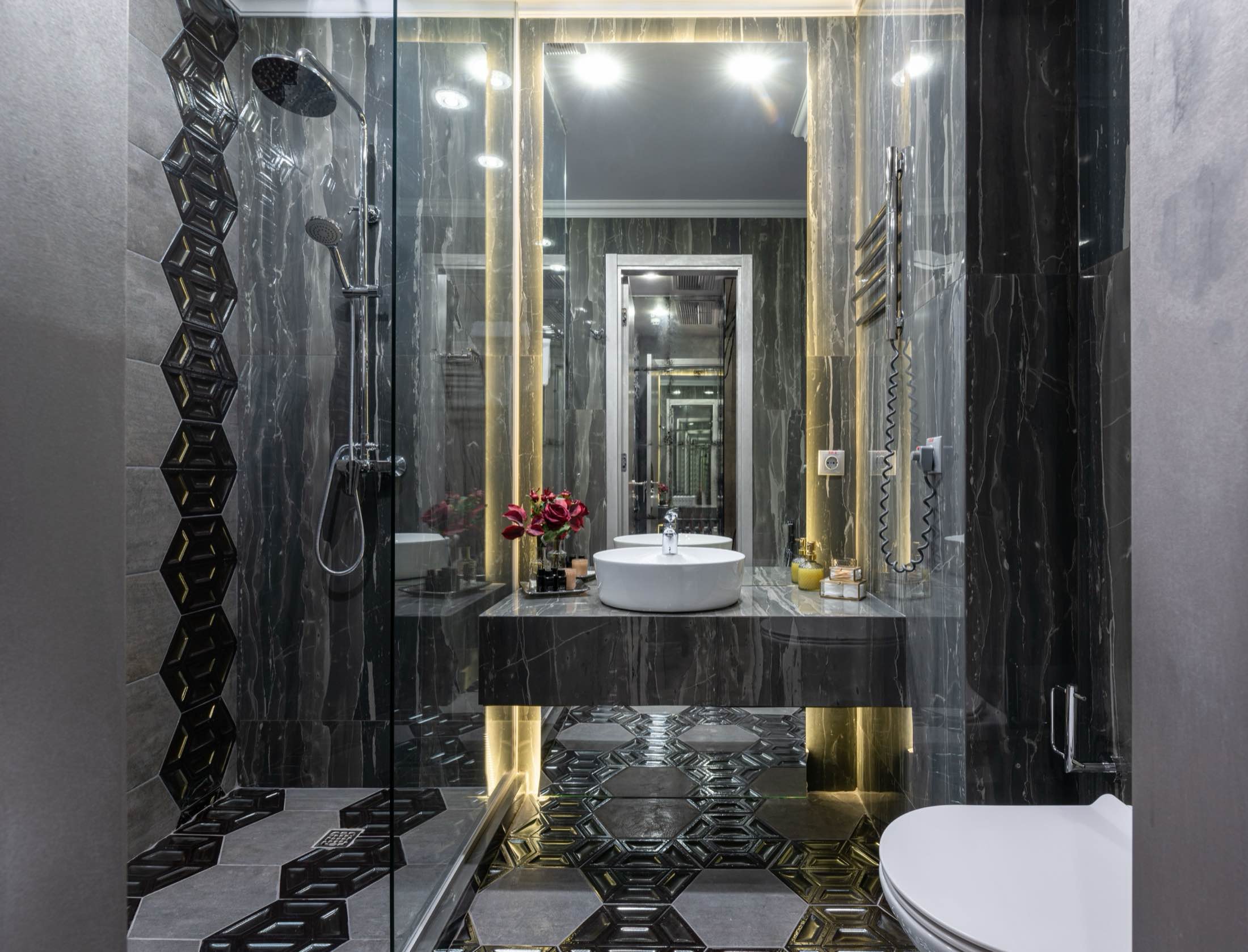 A walk-in shower finished in dark veined stone with brass trim and a rainfall head