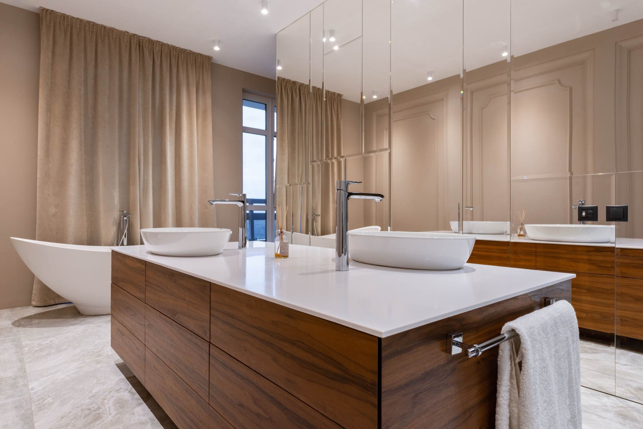 A bathroom with a walnut-clad vanity island, vessel basins and a freestanding tub