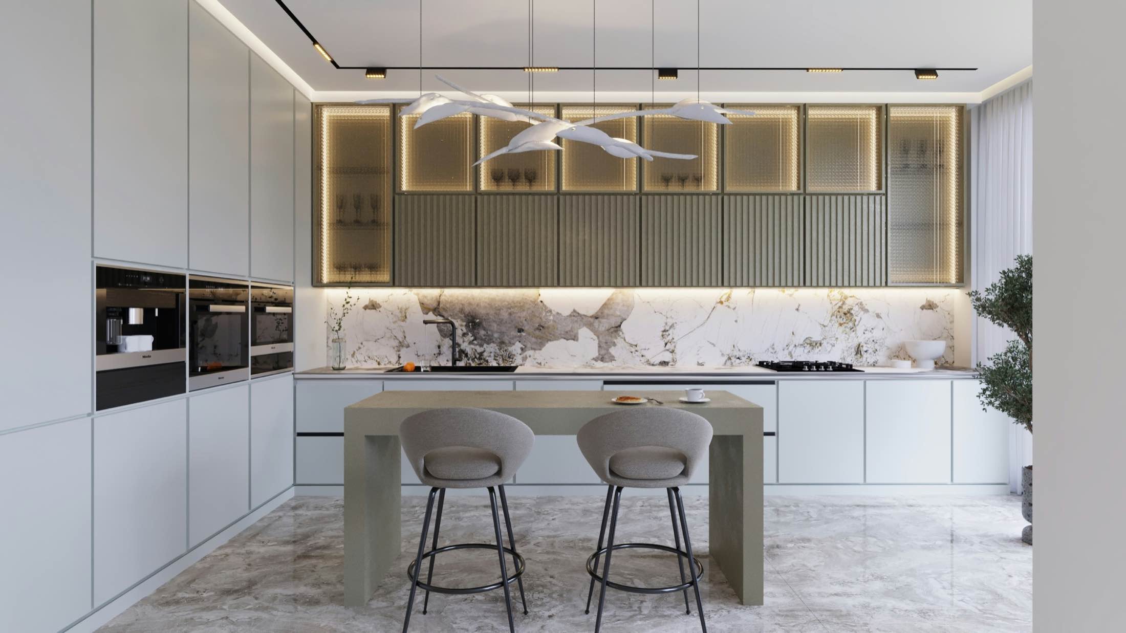 A kitchen with sage cabinetry, lit glass display units and a stone island