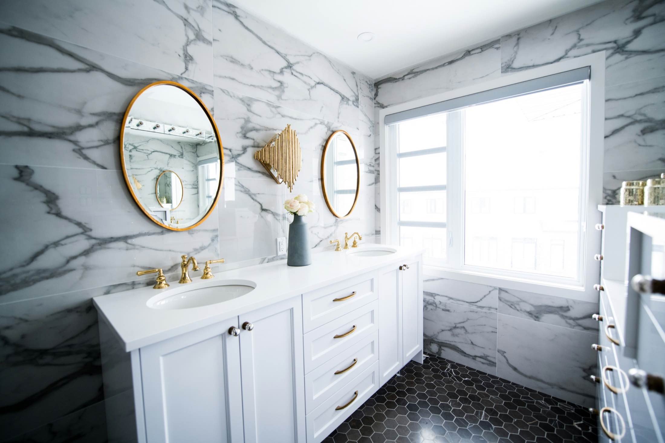 A marble bathroom with a white double vanity, brass fixtures and round gilt mirrors