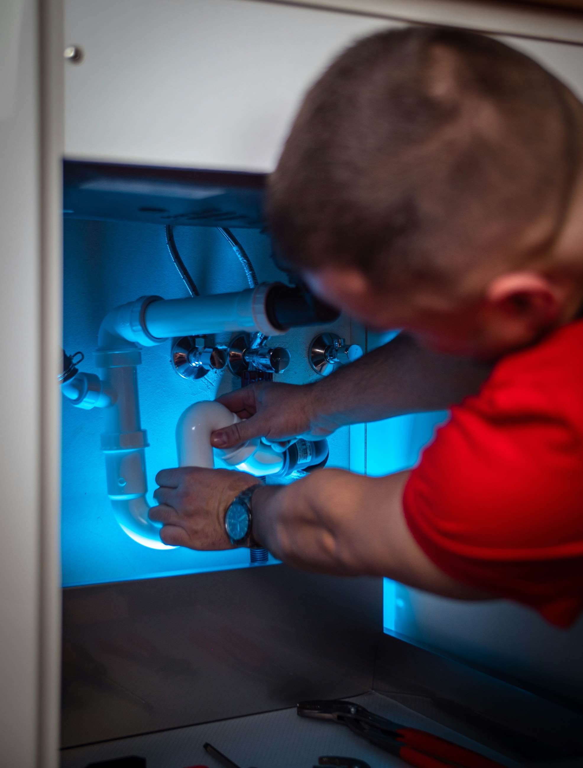 A plumber working on the trap and supply lines beneath a sink
